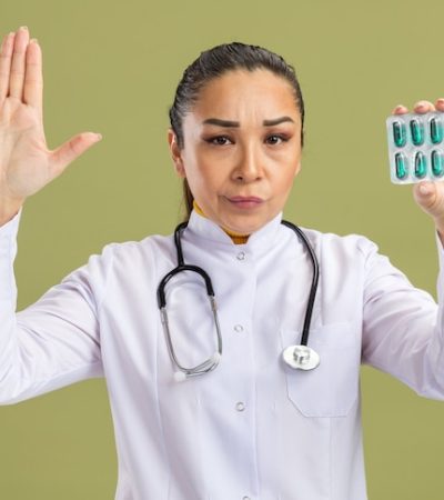 young-woman-doctor-white-medicine-coat-with-stethoscope-around-neck-holding-blister-with-pills-with-skeptic-expression-making-stop-gesture-with-hand-standing-green-wall_141793-100187